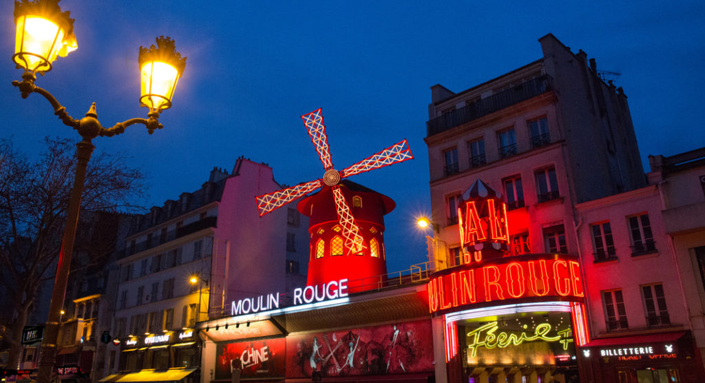 A store front at night with Moulin Rouge in the background