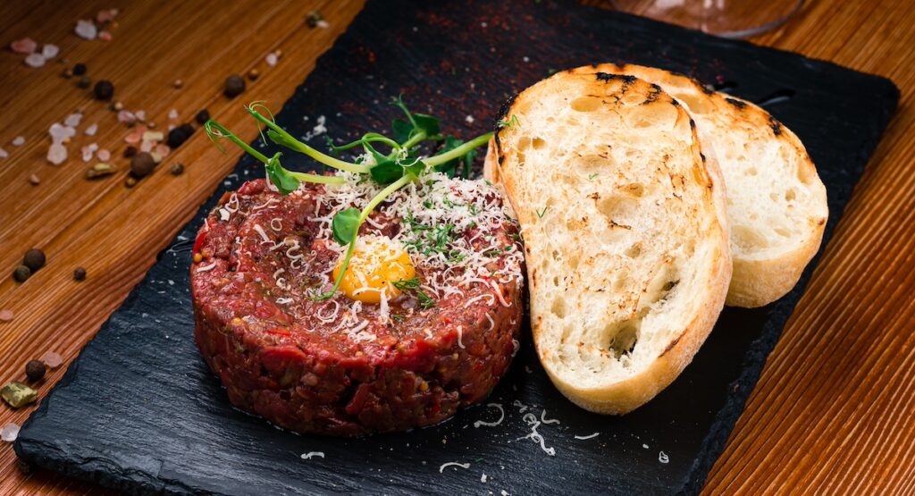 Beef steak tartare with raw egg yolk, pickled cucumber. French cuisine.