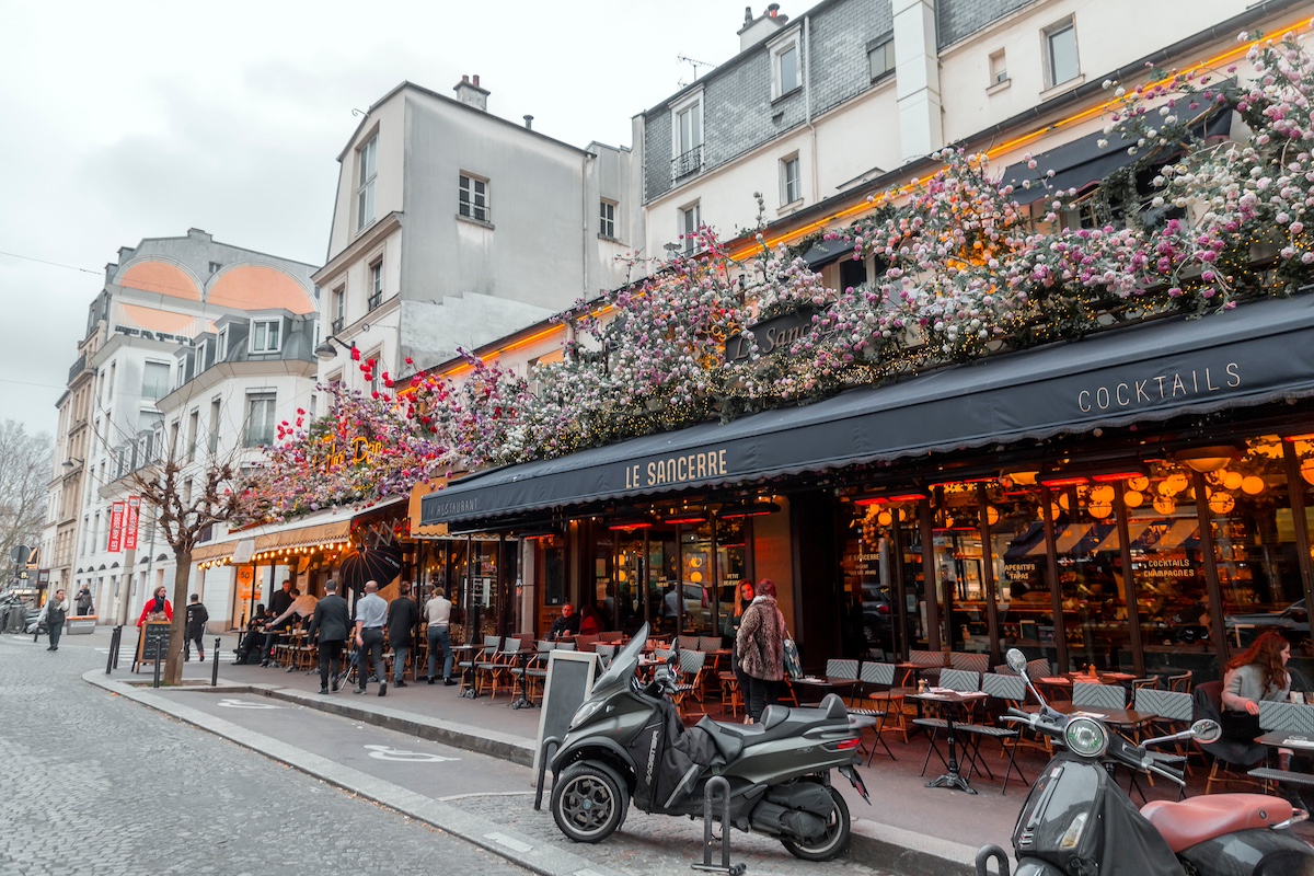 Paris, France - January 19, 2022: Typical Parisian cafe decorated with flowers and outside seats on Rue des Abbesses, Paris, France.