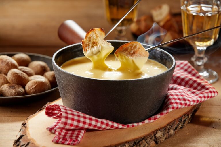 Steaming hot cheese fondue served with wine and toasted baguette on forks for dipping in close up on a rustic table