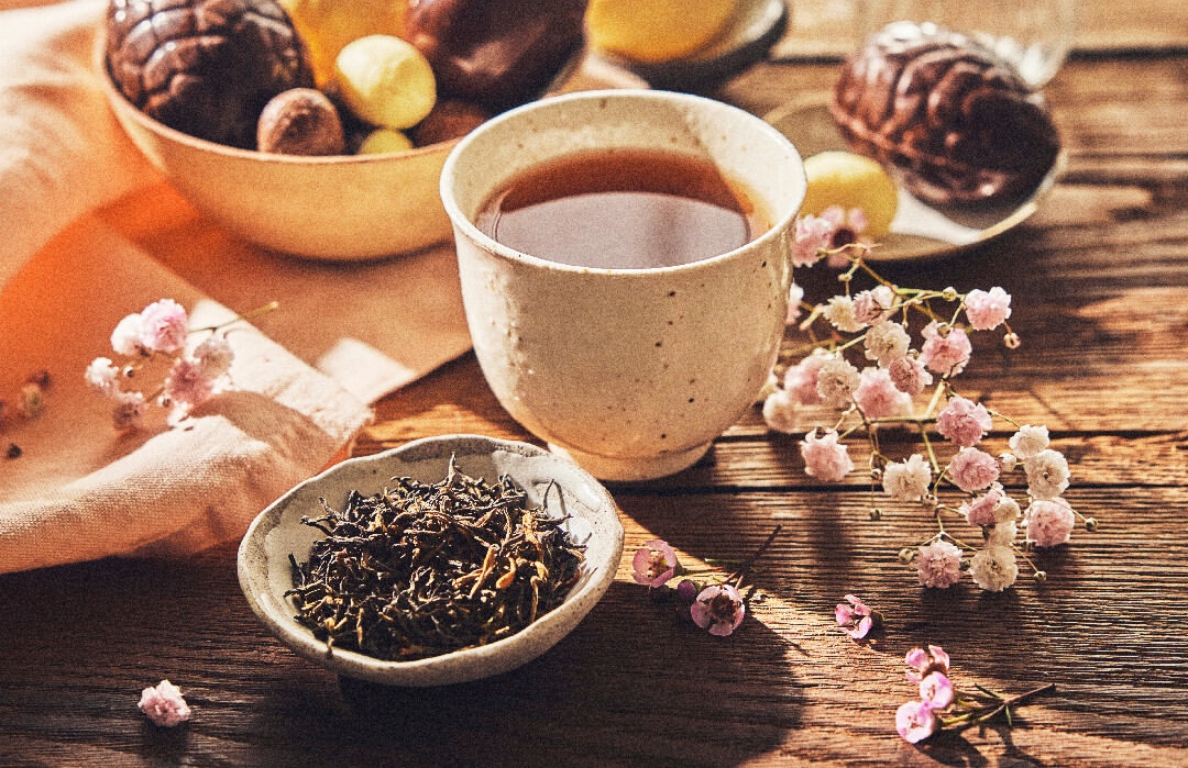 Cup of tea beside tea leaves and flower blossoms