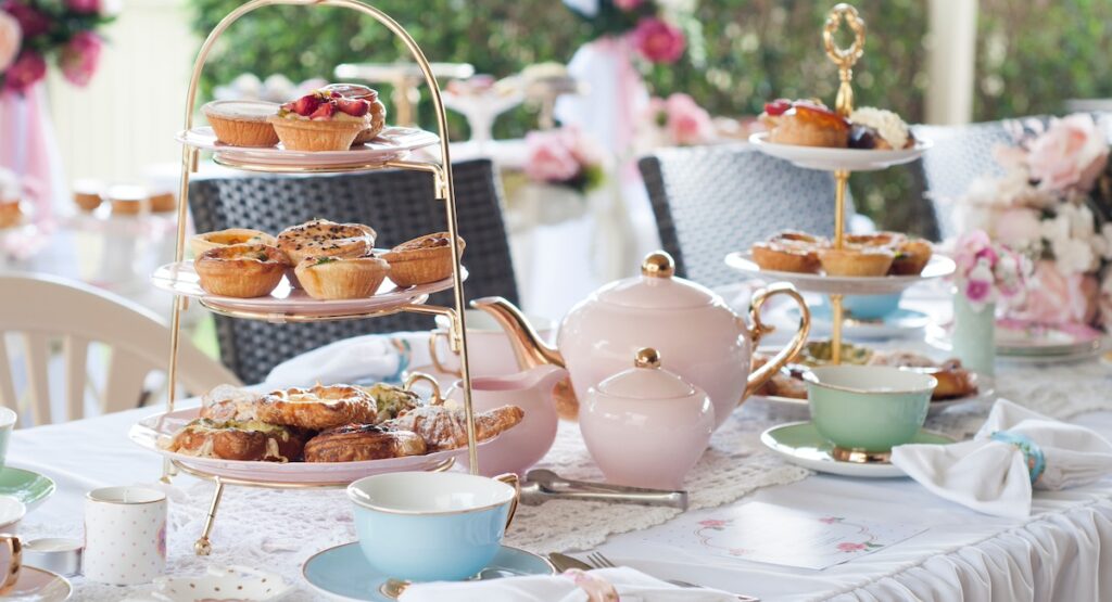 Pastel high tea set up featuring pastel pink, blue, yellow and green Royal Doulton tea set and an assortment of sweet and savoury pastries.