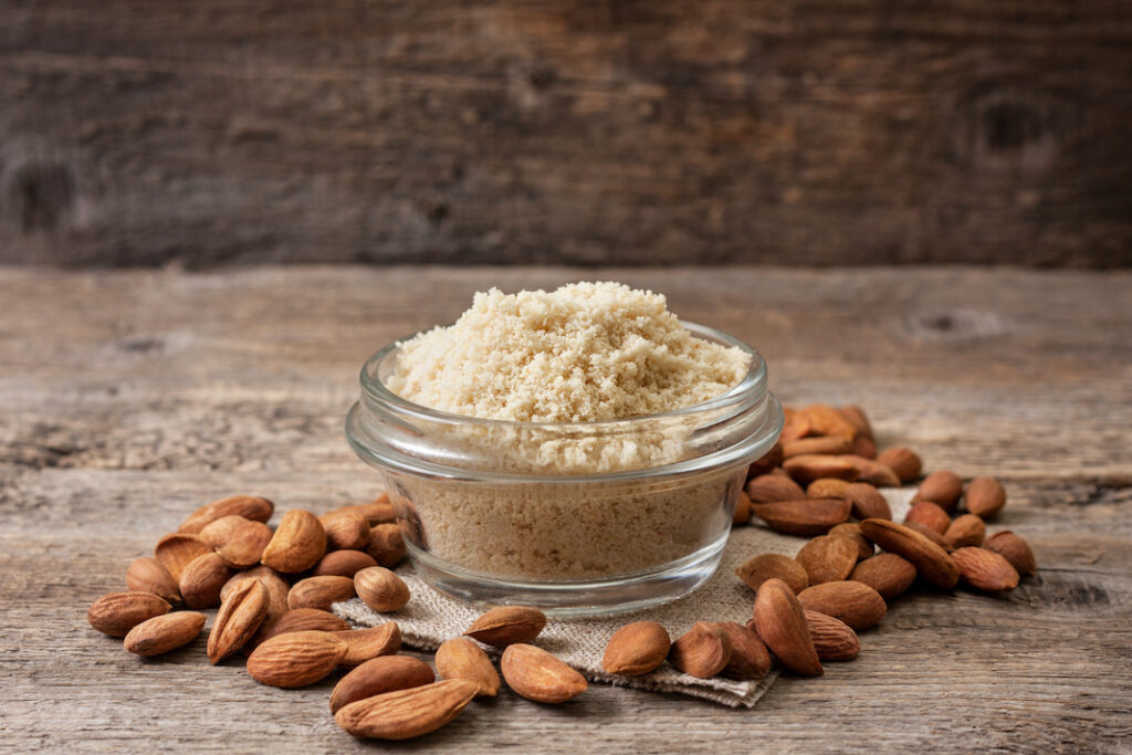 almond flour in a wooden bowl, almonds on old wooden background