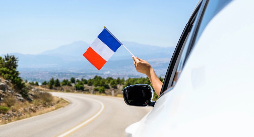 Woman holding France flag from the open car window driving along the serpentine road in the mountains.