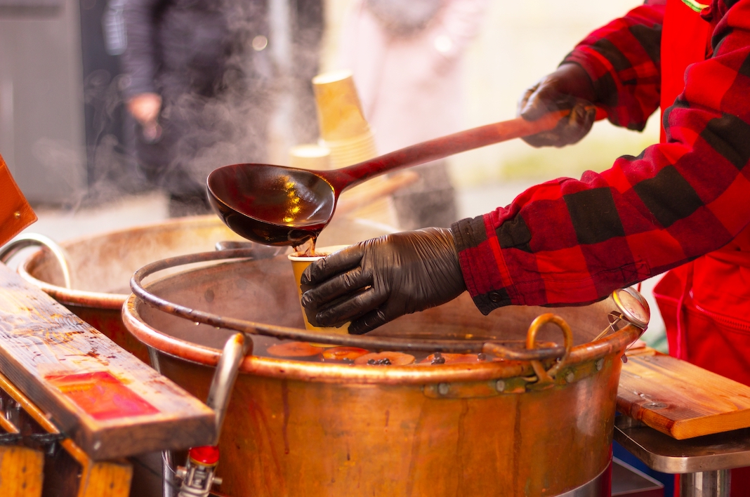 a man in red clothes pours mulled wine into a glass with a ladle, hands close-up. gluhwein, hot drink. winter holidays.