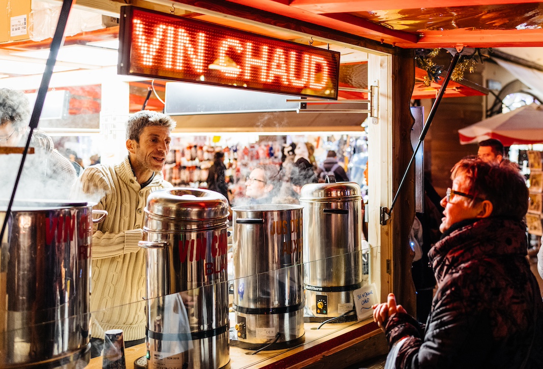 STRASBOURG, FRANCE - NOV 29, 2017: happy French woman buying mulled wine from Market stall in the evening during Strasbourg Christmas Market in Place de la Cathedrale, Alasace