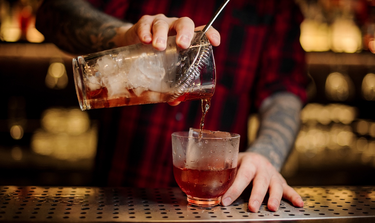 Bartender pouring a delicious Vieux Carre cocktail from the measuring cup to a glass on the bar counter