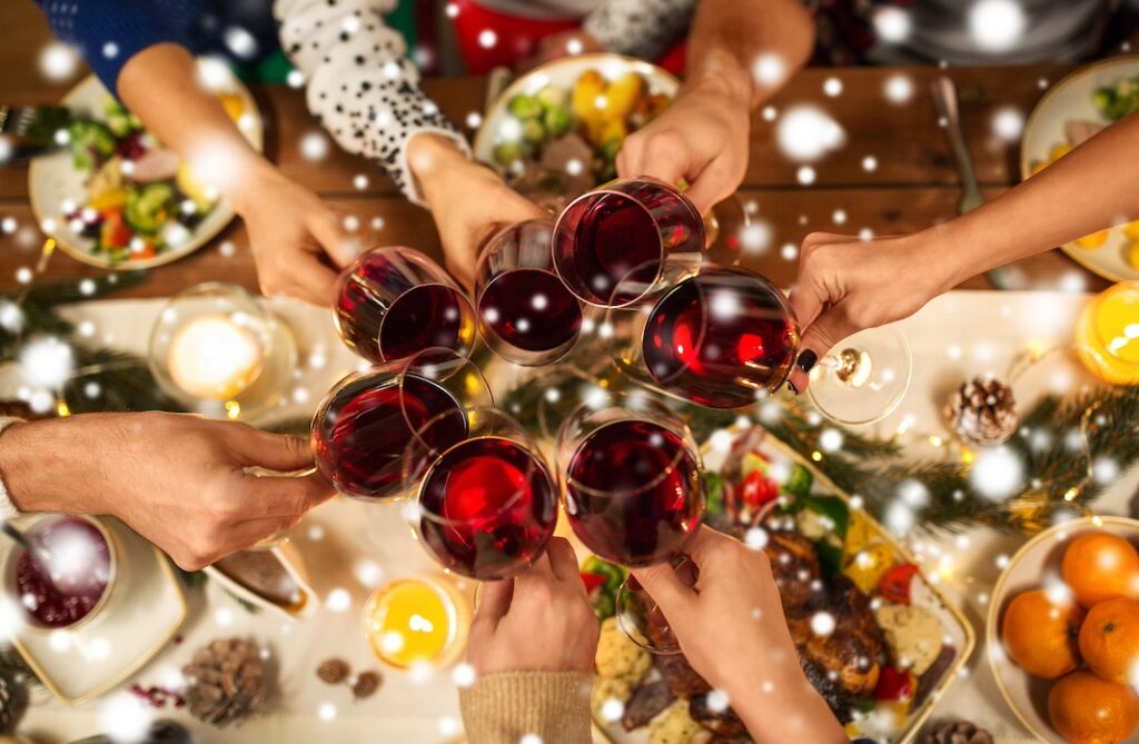 People toasting with red wine glasses over table of Christmas decorations