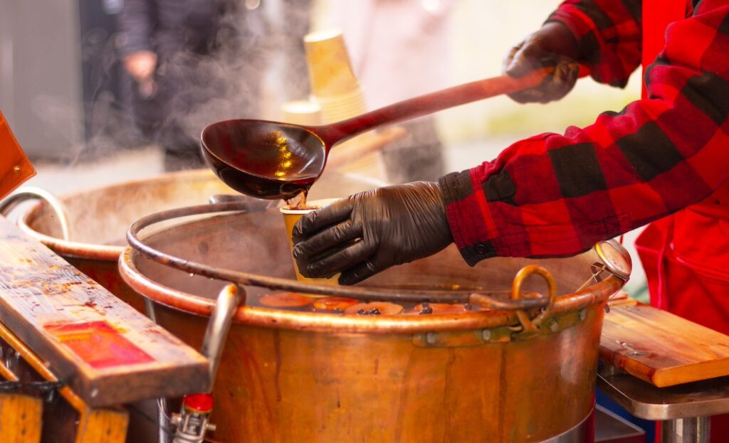 a man in red clothes pours mulled wine into a glass with a ladle, hands close-up. gluhwein, hot drink. winter holidays.