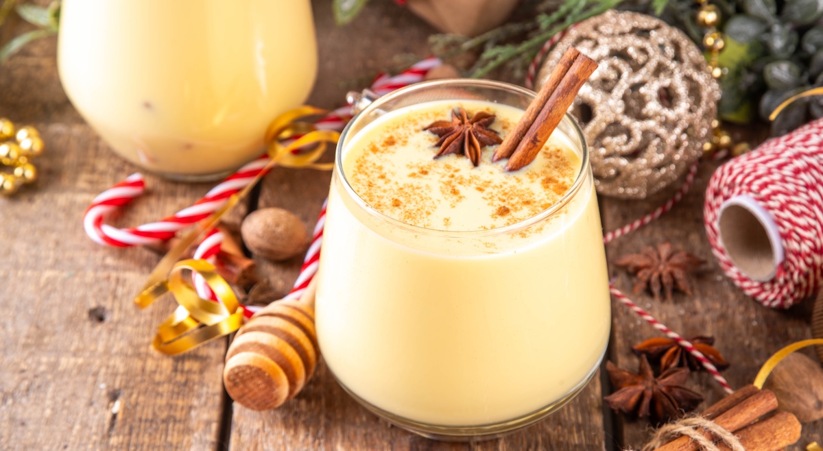 Christmas drink with cinnamon sticks and anise stars, two glasses of sweet classic eggnog cocktail on Christmas, New Year decorated background with fir tree and baubles