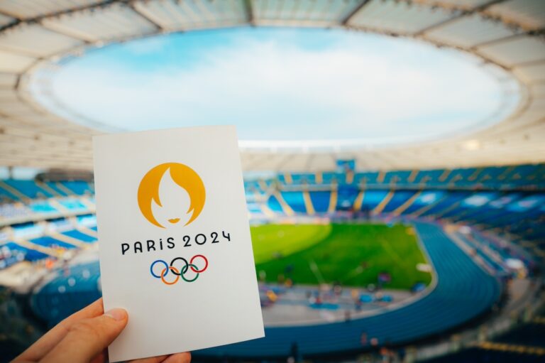 PARIS, FRANCE, JULY 7, 2023: Icon of Summer olympic Games Paris 2024 Held by Athlete. Modern Olympic Stadium in background. Wallpaper for Summer Olympic Game in Paris 2024.