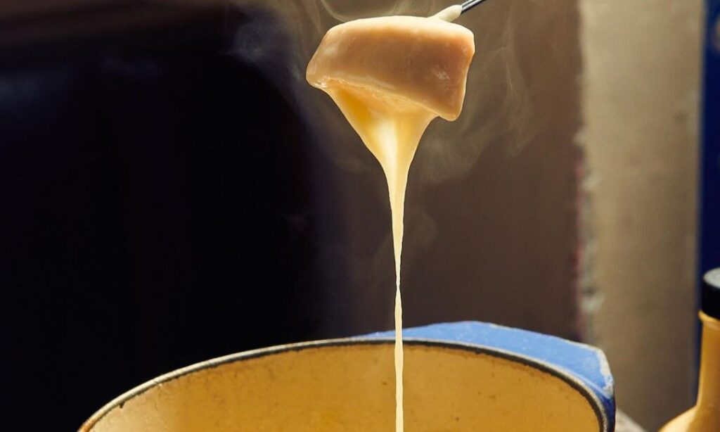 Piece of bread dripping with melted cheese over fondue pot
