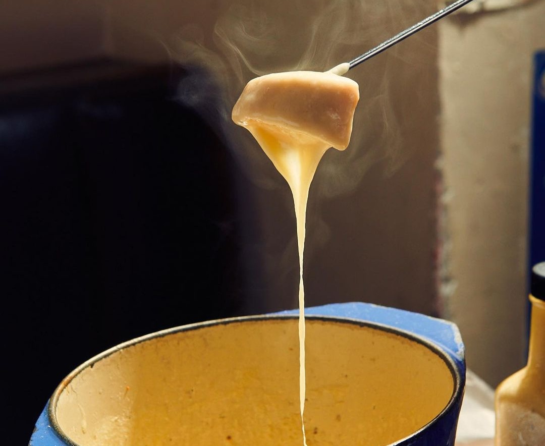 Piece of bread dripping with melted cheese over fondue pot