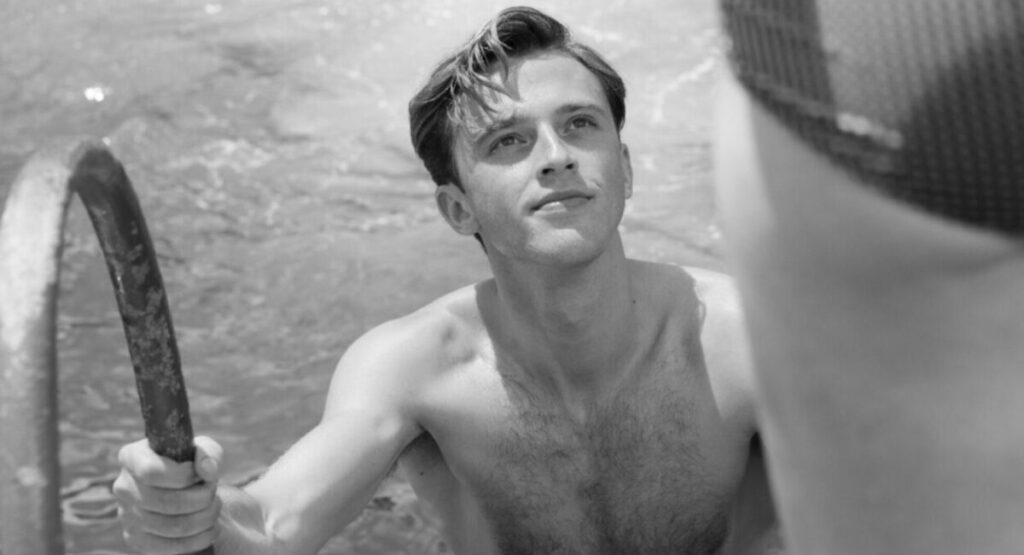 A man climbs out of a swimming pool looking up at a woman