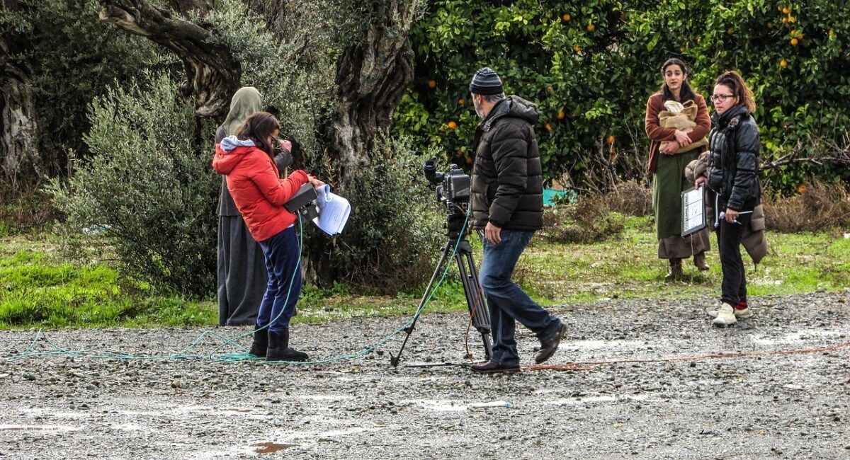 Film crew shooting on dirt road by forest.