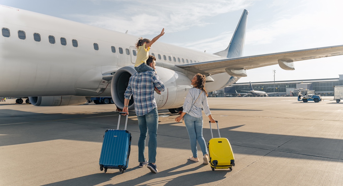 Back view of happy family standing near a large plane with two suitcases outdoors.