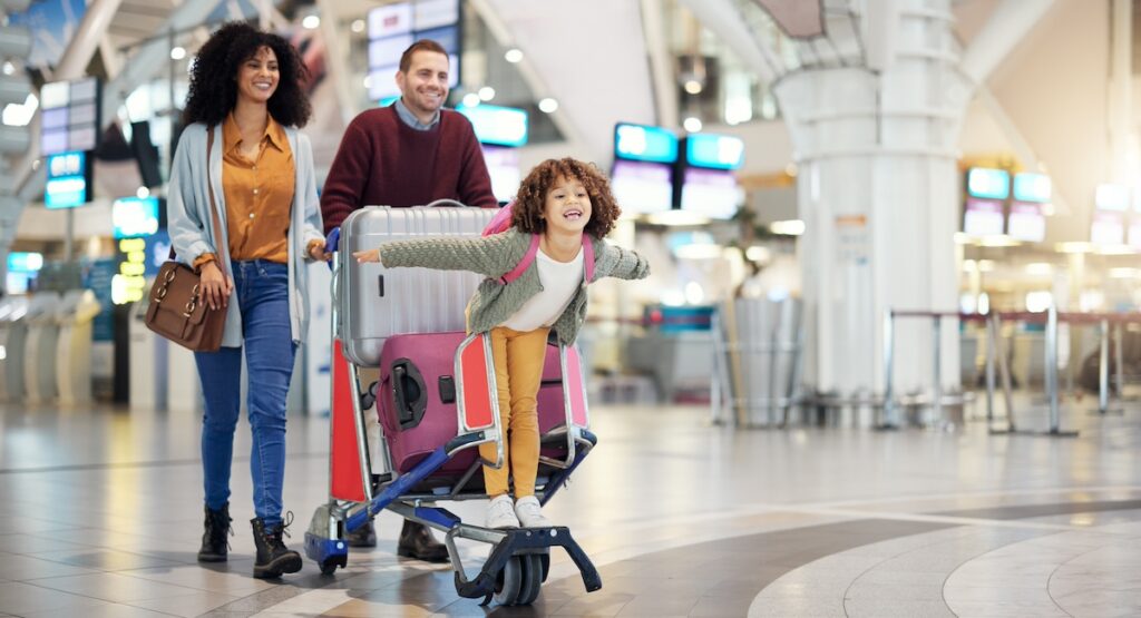 Airport, family and child excited for flight with suitcase trolley on holiday, vacation or immigration journey and travel. Luggage of mother, father or diversity parents with girl kid flying in lobby