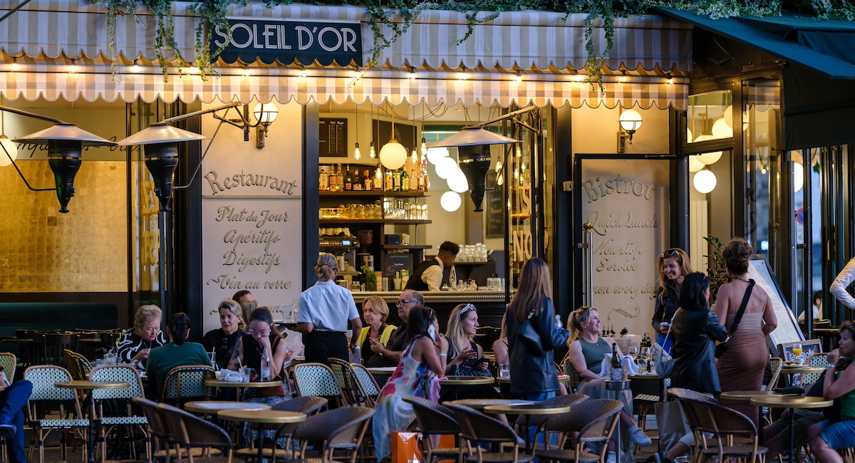 View of people sitting outdoors and enjoying dinner and drinks at a restaurant bistro in Paris France.