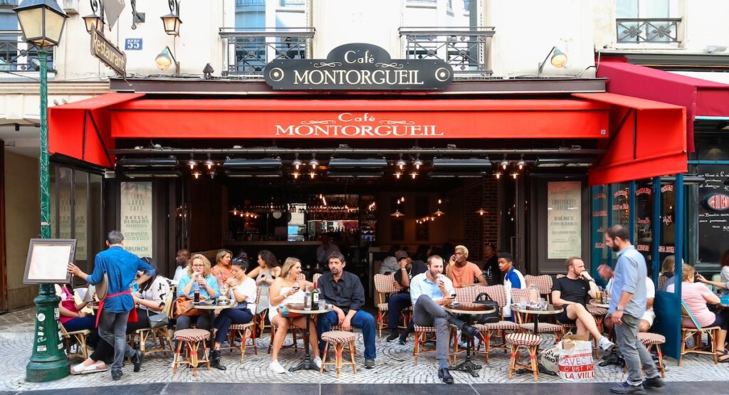 PARIS - AUGUST 23, 2017: People passes by a cafe on Rue Montorgueil street. People have brunch/lunch at cafe and enjoy nice weather on August 23, 2017.