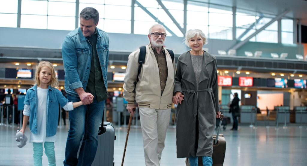 Full length of delighted old grandparents are going with their son and granddaughter at airport terminal to check-in on their flight.