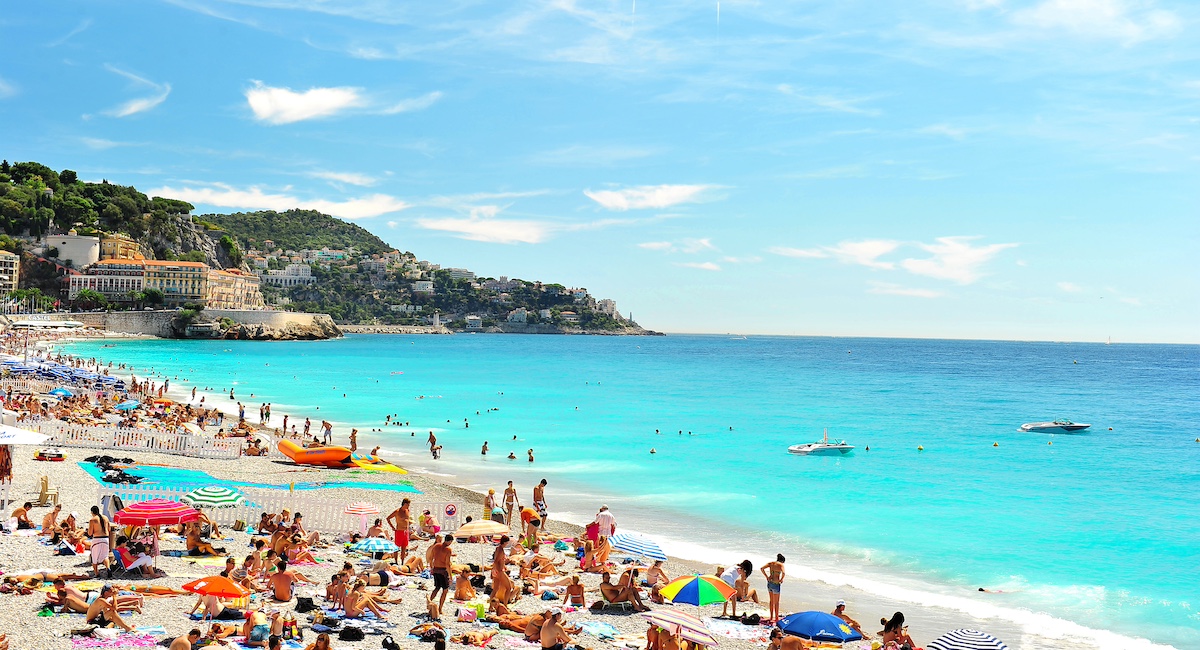 View of the beach in Nice, France, near the Promenade des Anglais. tourists, sunbeds and umbrellas on summer hot day