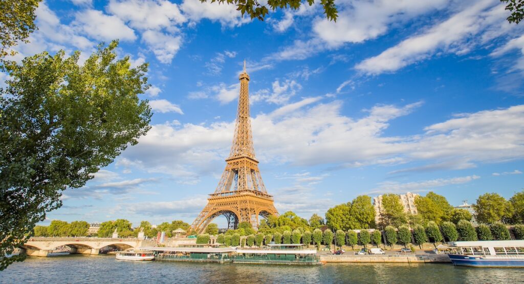 A panoramic view of the Eiffel Tower against a background of blue sky and beautiful clouds and the Seine River on a sunny day in Paris.