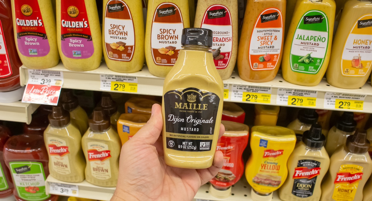 A view of a hand holding a bottle of Maille dijon mustard, on display at a local grocery store.