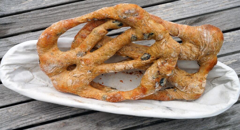 A couple of fougasse aux olives served on a white dish that sits on top of a wooden table