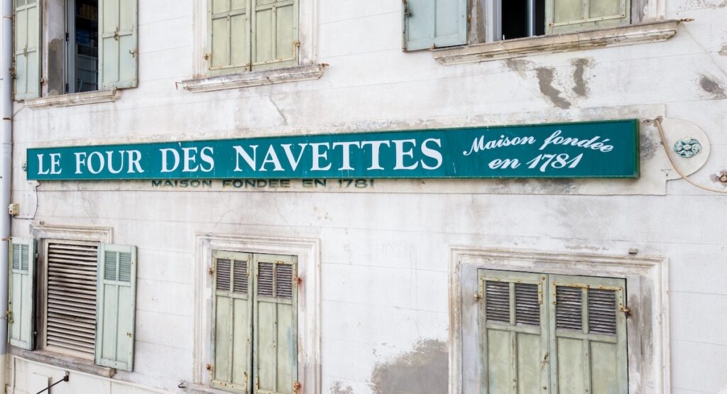A green sign that reads "Four des Navettes, maison fondée en 1781" on the side of an old building in Marseille.