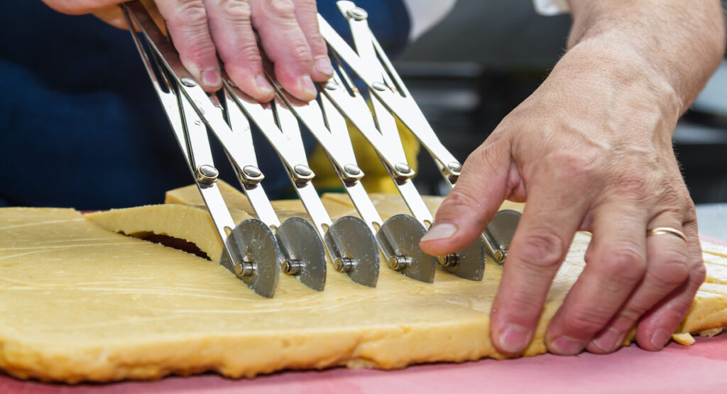 close up of a chefs hands slicing equal individual servings of panisses with a special cutting tool