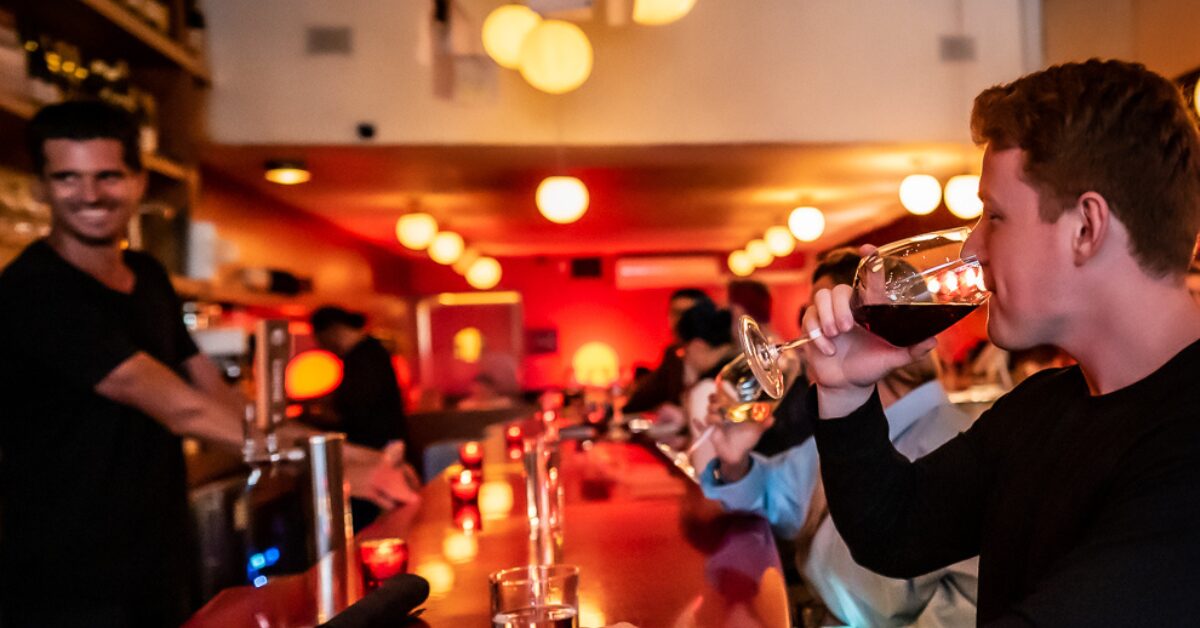 Man drinking wine at warmly lit red wine bar