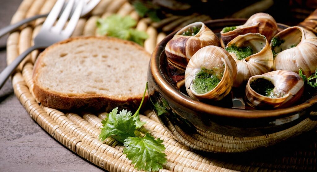 Escargots de Bourgogne - Snails with herbs butter, gourmet dish, in two traditional ceramic pans with coriander and bread on straw napkin.