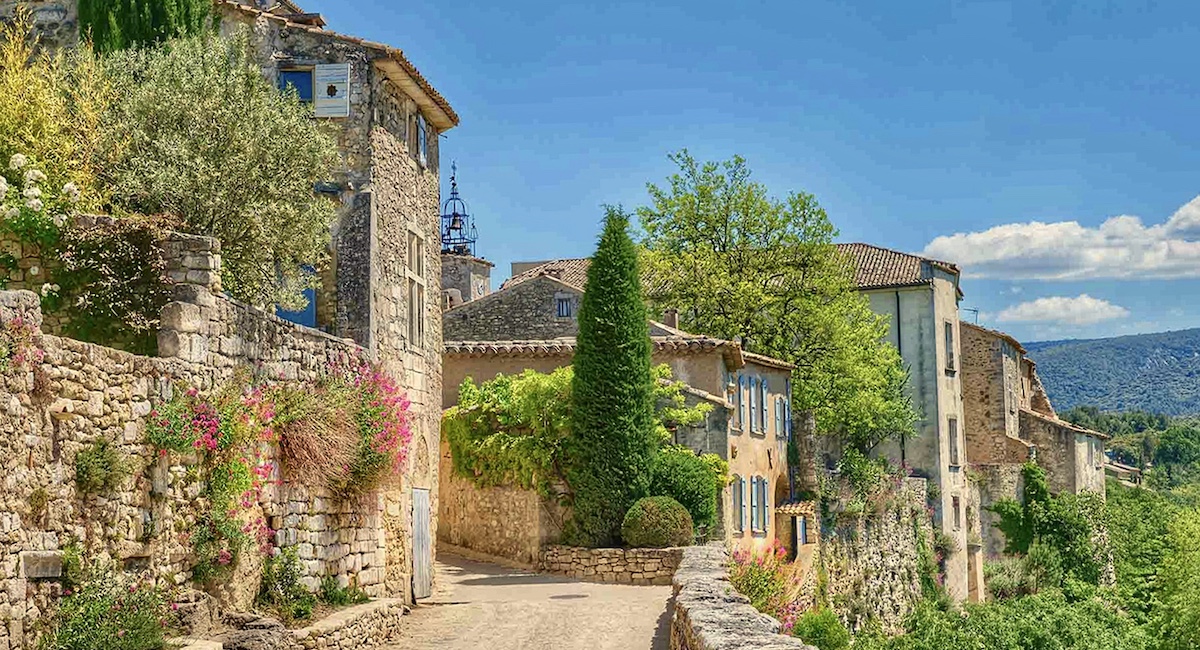 Road lined with stone wall leading to houses in Menerbes