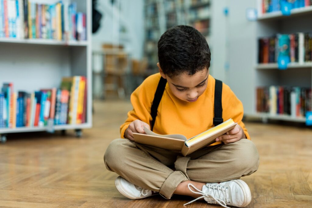 Little boy sitting on the floor in a library, reading a book