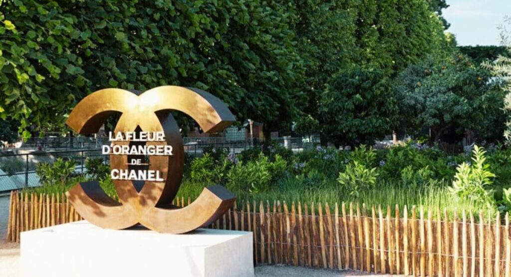 Large gold Chanel logo against greenery.