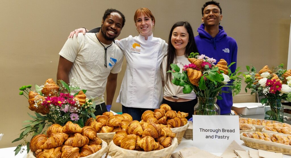 Bakers posing behind a table of croissants.
