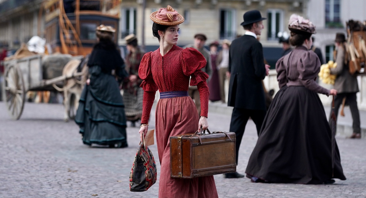 Woman dressed in old fashioned red dress, carrying briefcase through city streets