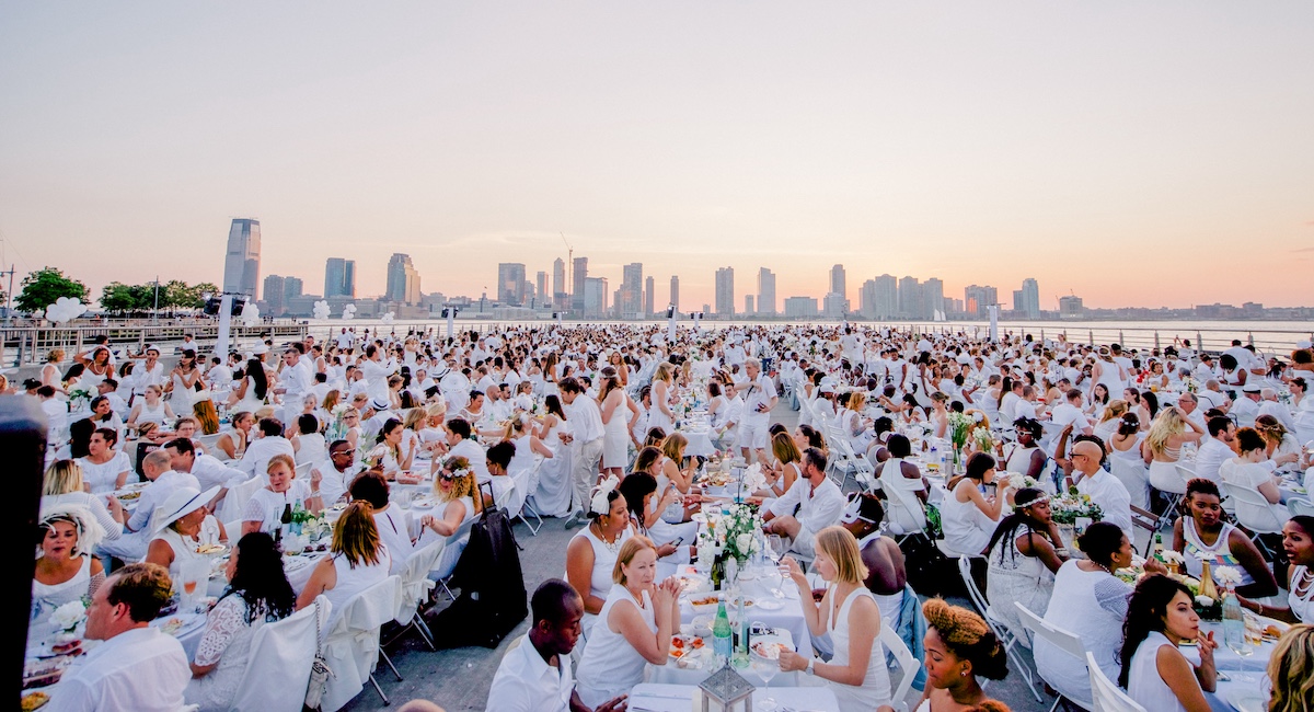 Hundreds of people dressed in white beside the waterfront at sunset