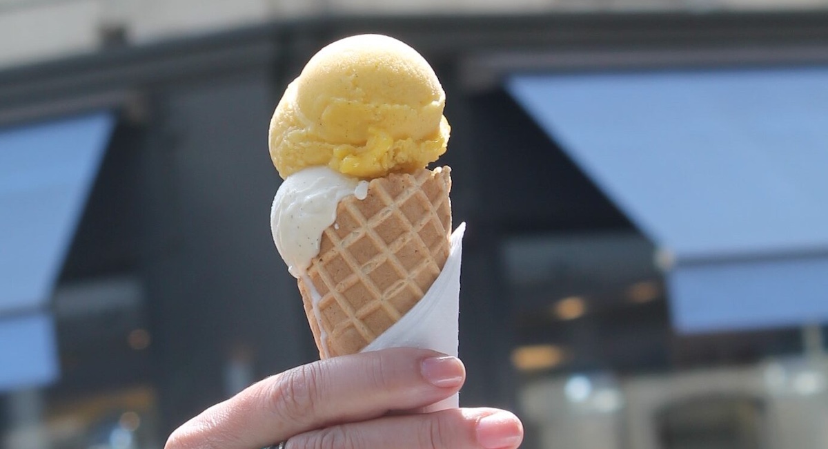 Hand holding ice cream cone in scoops of orange and white