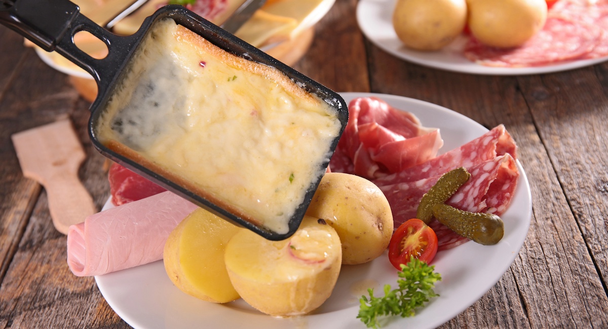 Melted Raclette being scraped over potatoes and charcuterie