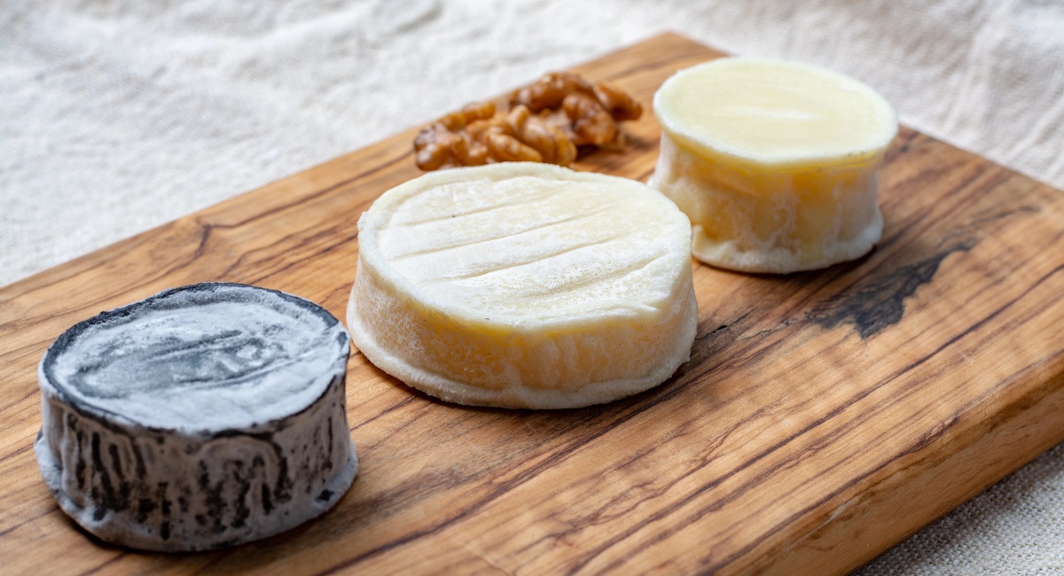 Assortment of French soft goat cheeses, Chevre Cendre, Cabecou Du Perigord and Chevre De Dordogne served on olive tree board close up