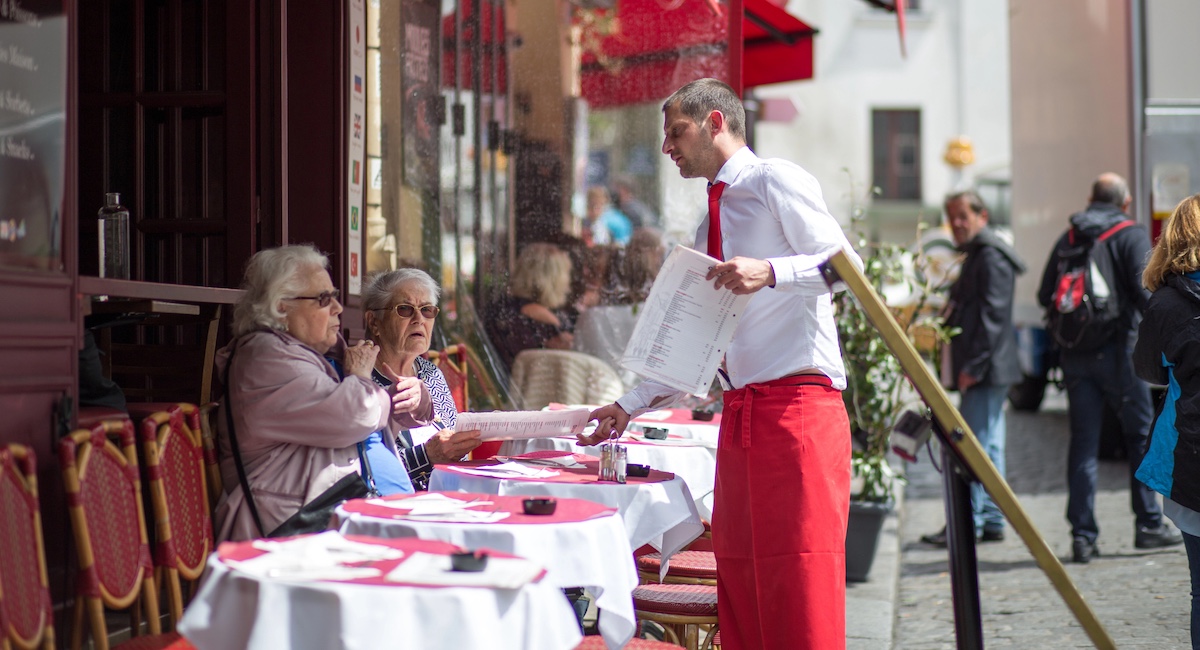 A waiter serving customers in the outside area of a restaurant in Montmartre district