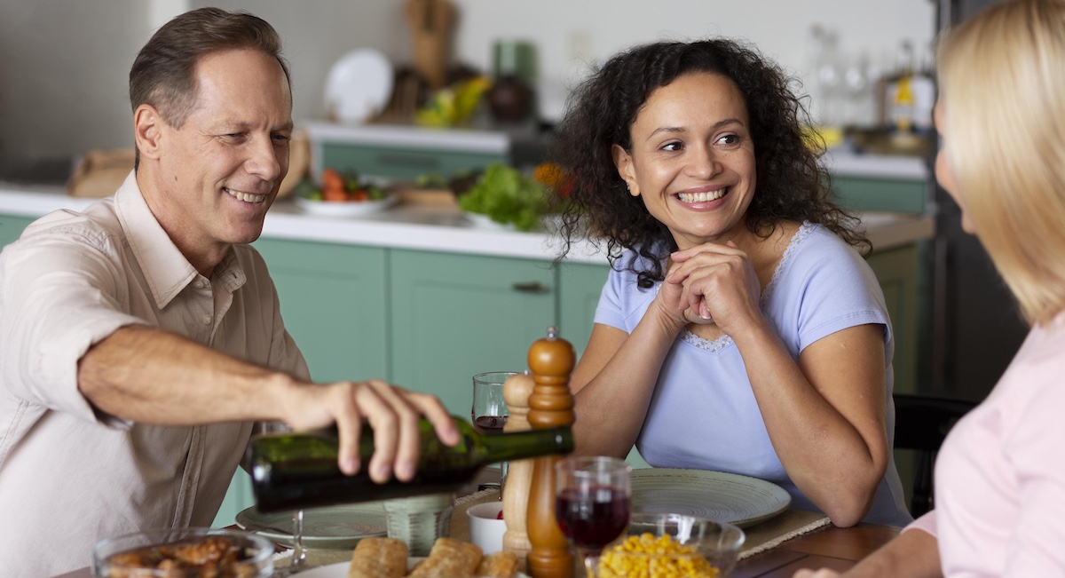 Smiling couple shares dinner and pours wine for blonde woman
