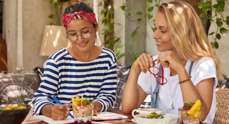 Young woman doing homework at breakfast table while her teacher looks on and smiles