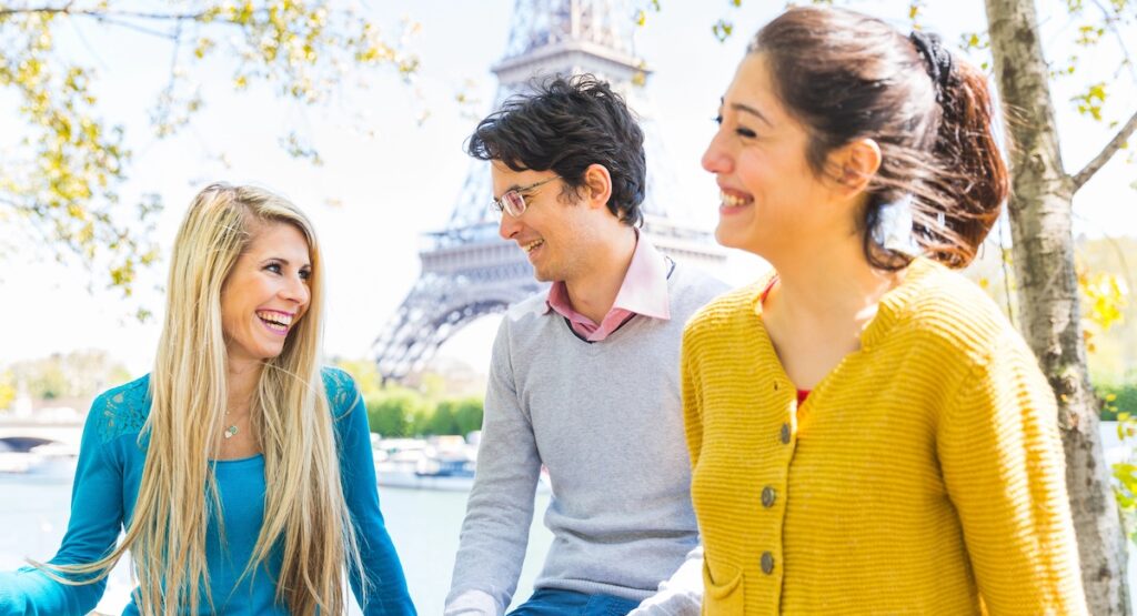Three joyful friends enjoying time together in a sunny park in Paris by Seine river and Eiffel tower - Friends laughing and spending time outdoors in Paris