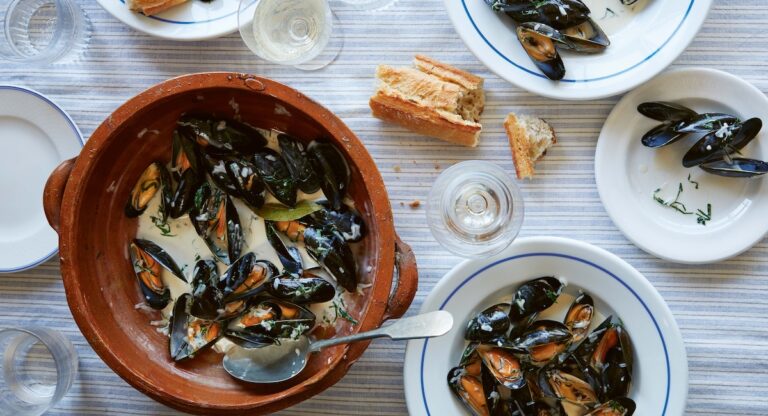 Moules marinieres, bread, and white wine on table