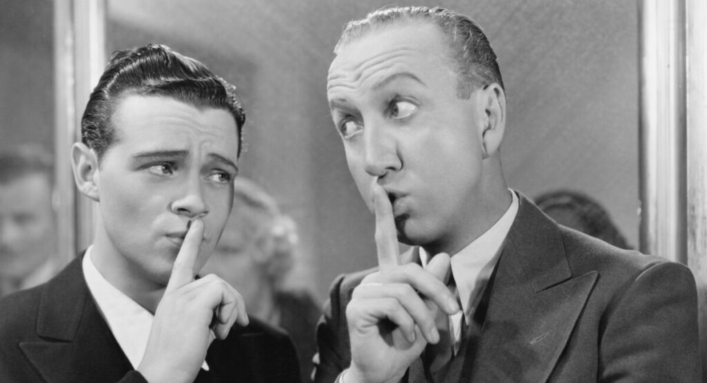 Two men making a shushing gesture in black and white.