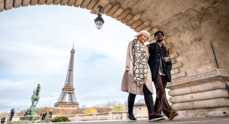 Couple walking under bridge by Eiffel Tower.