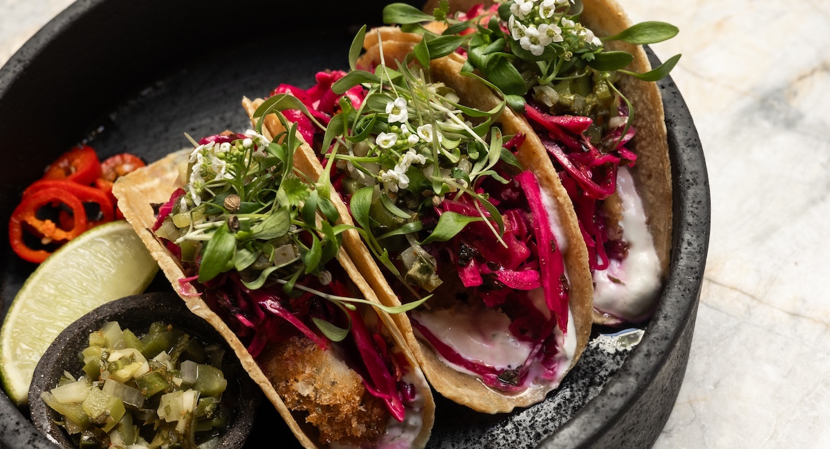 Tacos plated on black plate with flower garnishes.