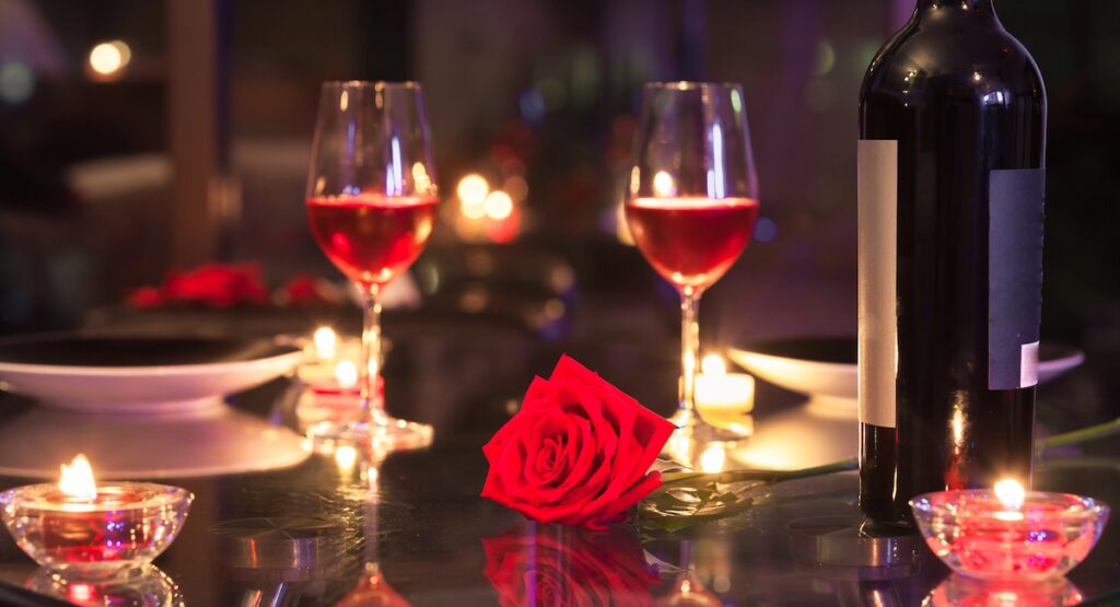 Candlelit dinner set with roses and two glasses of wine.